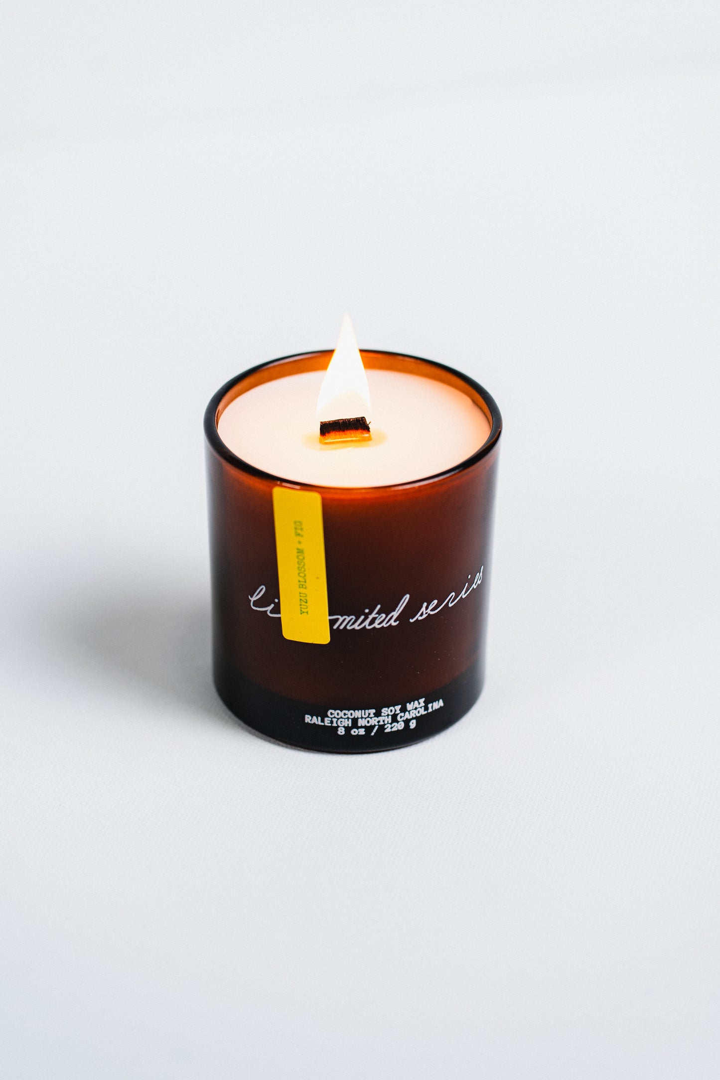 Candle in a brown glass jar with a yellow label on a white background